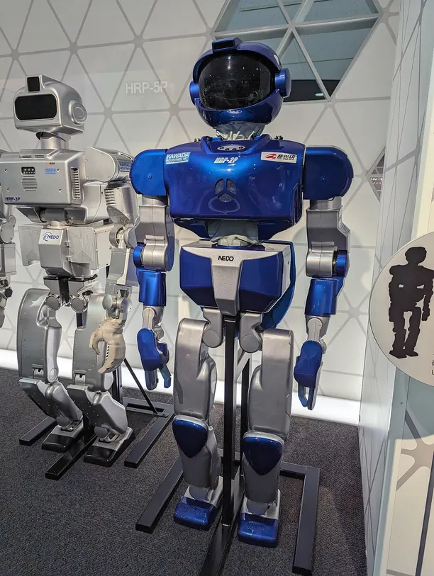 Robô humanoide azul e branco em exposição num museu de ciência, de pé sobre um suporte