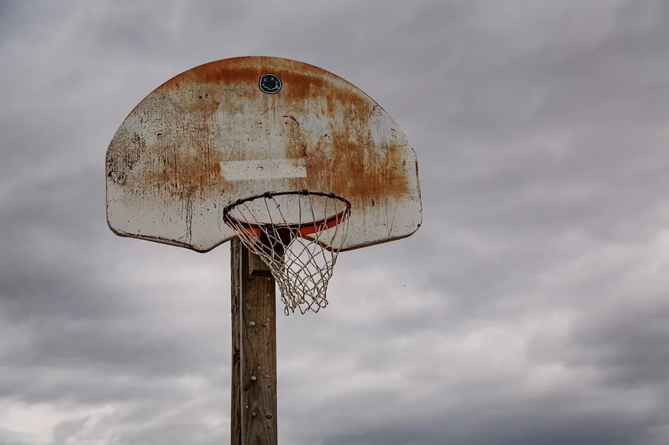 Tabela de basquetebol ferrugenta presa a um poste de madeira, sob céu cinzento carregado